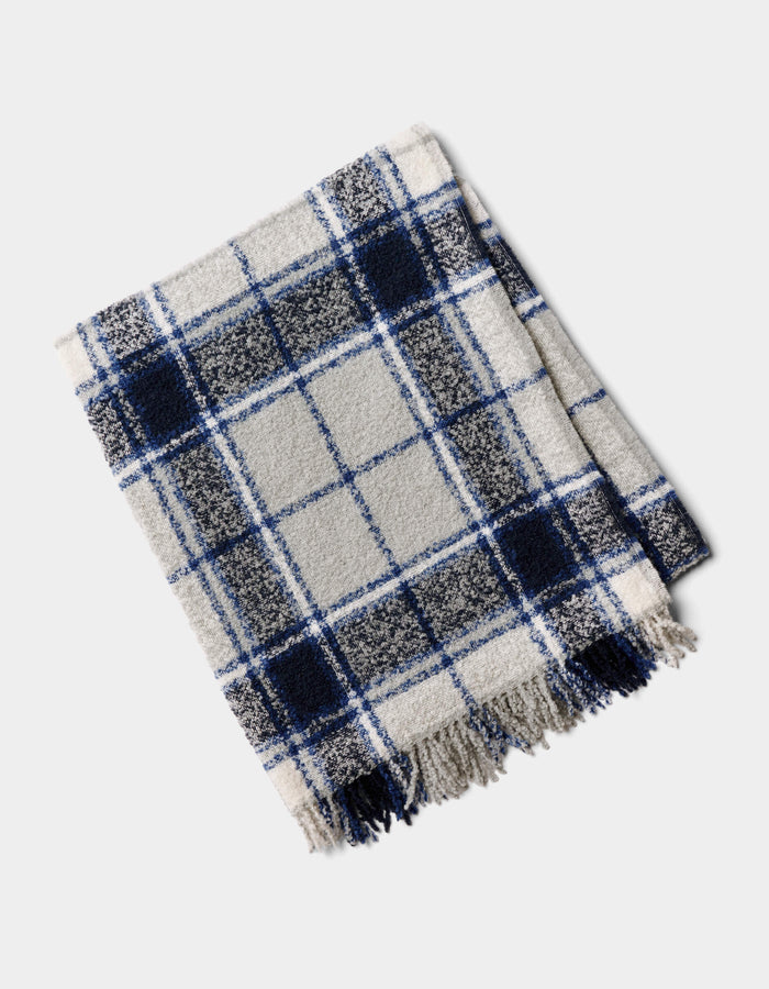 The Cozy Earth Alpaca Boucle Throw, featuring a blue, black, and white plaid design with fringed edges, is shown folded on a light background.|Color:Indigo Plaid