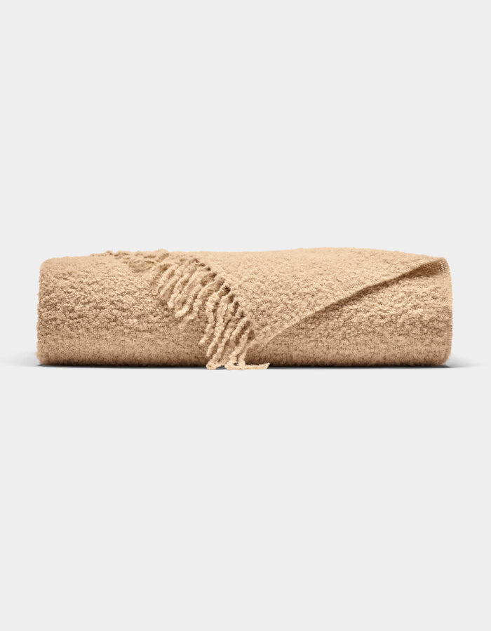 The Cozy Earth Alpaca Boucle Throw, featuring a textured surface and fringed edges in beige, is neatly folded and displayed against a plain white background.|Color:Sandalwood