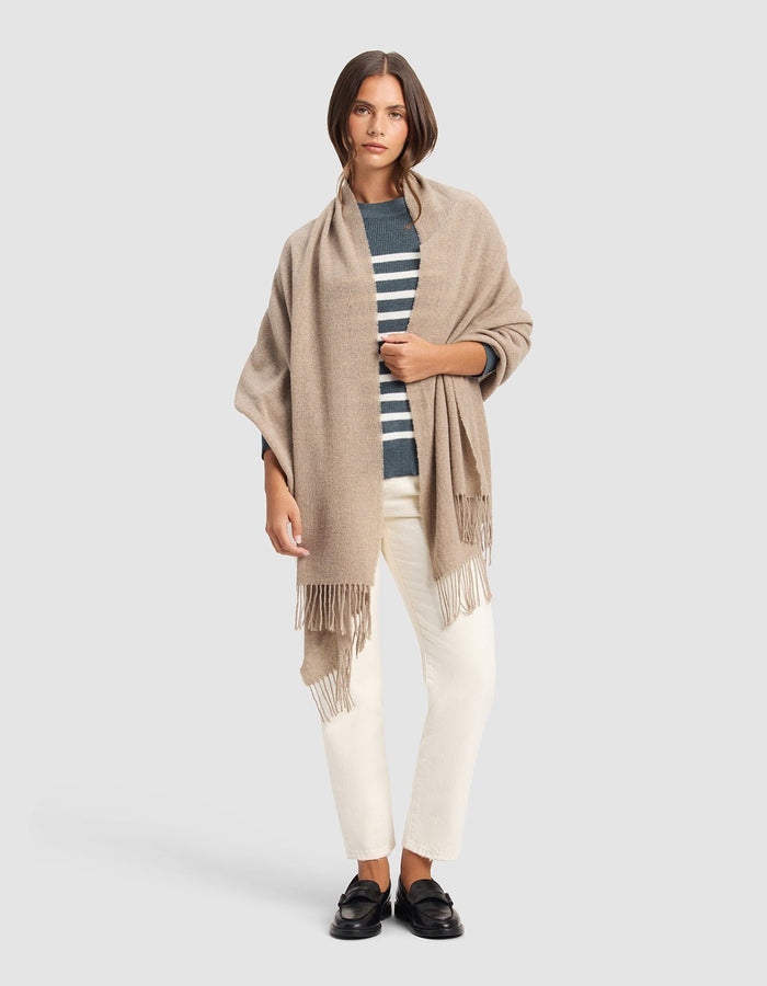 A woman with straight brown hair and a neutral expression stands against a plain background wearing the Cozy Earth Amelia Wrap, a navy and white striped sweater, off-white pants, and black loafers.|Color:Taupe