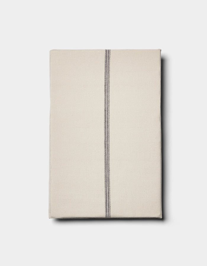 The Cozy Earth Baja Double Sided Sham is shown neatly folded in beige, featuring a single off-center vertical black stripe, set against a plain light background.|Color:Coal Stripe/Striped Alabaster