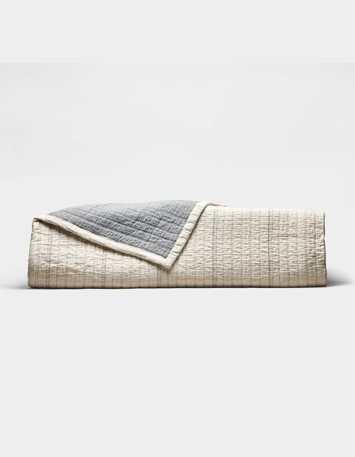 The Cozy Earth Baja Matelasse Coverlet features a neatly folded design with a cream side adorned with subtle lines and a textured gray reverse, shown against a plain white background.|Color:Alabaster/Oceanside