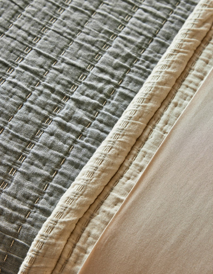 Close-up of the Cozy Earth Baja Matelasse Coverlet, featuring a stitched geometric texture, cream border, and smooth light beige fabric alongside.|Color:Alabaster/Oceanside