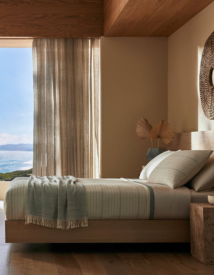 A serene bedroom features the Cozy Earth Baja Matelasse Bundle, soft neutral bedding, and decorative pillows. Light beige curtains are partially open to an ocean view, with natural light filling this cozy, minimalist space.|Color:Alabaster/Oceanside