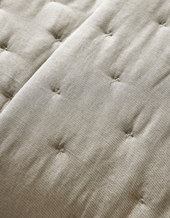 Close-up of the Cozy Earth Baja Quilt’s beige, textured surface featuring parallel lines and button-like tufts for a quilted, cushioned look.|Color:Coal Stripe/Striped Alabaster
