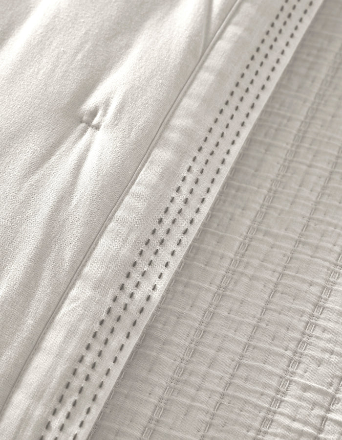 Close-up of the Cozy Earth Baja Quilt in white, featuring quilted stitching and a decorative perforated hem that highlights the soft, textured woven details.|Color:Laurel Stripe/Striped Bone