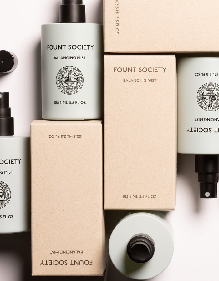 An array of Balancing Face Mist bottles by Cozy Earth, along with their packaging boxes, arranged aesthetically. The light blue-green bottles feature black spray nozzles and are labeled with the brand name "Cozy Earth," product name "Balancing Face Mist," and size (103.5 mL, 3.5 FL OZ). |Size:Full Size