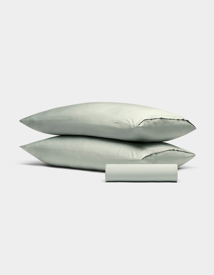 The Cozy Earth Bamboo Bedding Basic Bundle features two light gray pillows stacked together with a matching pillowcase rolled in front, all displayed against a plain white background.|Color:Laurel