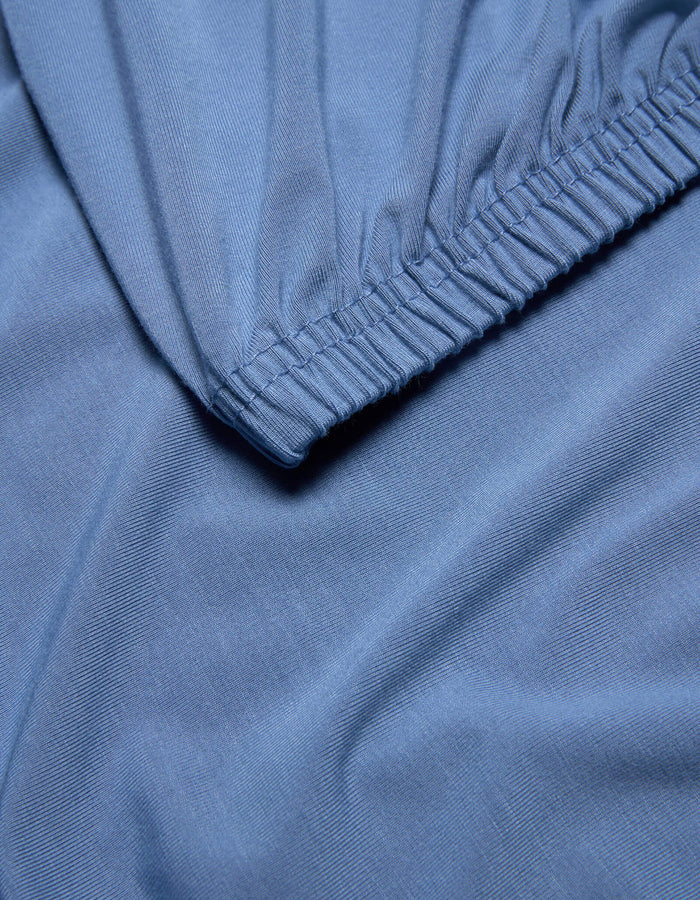 Close-up of light blue Bamboo Jersey Fitted Sheet by Cozy Earth, featuring an elastic edge, smooth texture, and gentle folds.|Color:Sailor