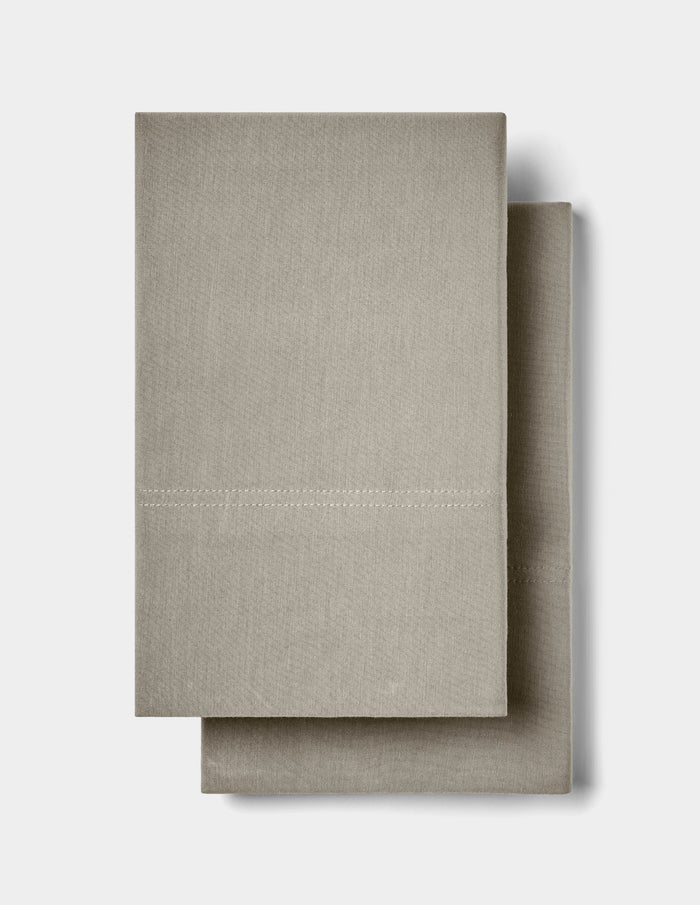 Two neatly folded, light beige Bamboo Jersey Pillowcases by Cozy Earth stacked on top of each other against a plain white background.|Color:Stone
