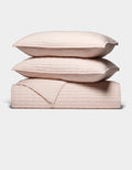 The Cozy Earth Bamboo Jersey Quilt Bundle features two light pink quilted pillows stacked atop a matching quilted blanket, all neatly arranged against a plain white background.|Color:Petal