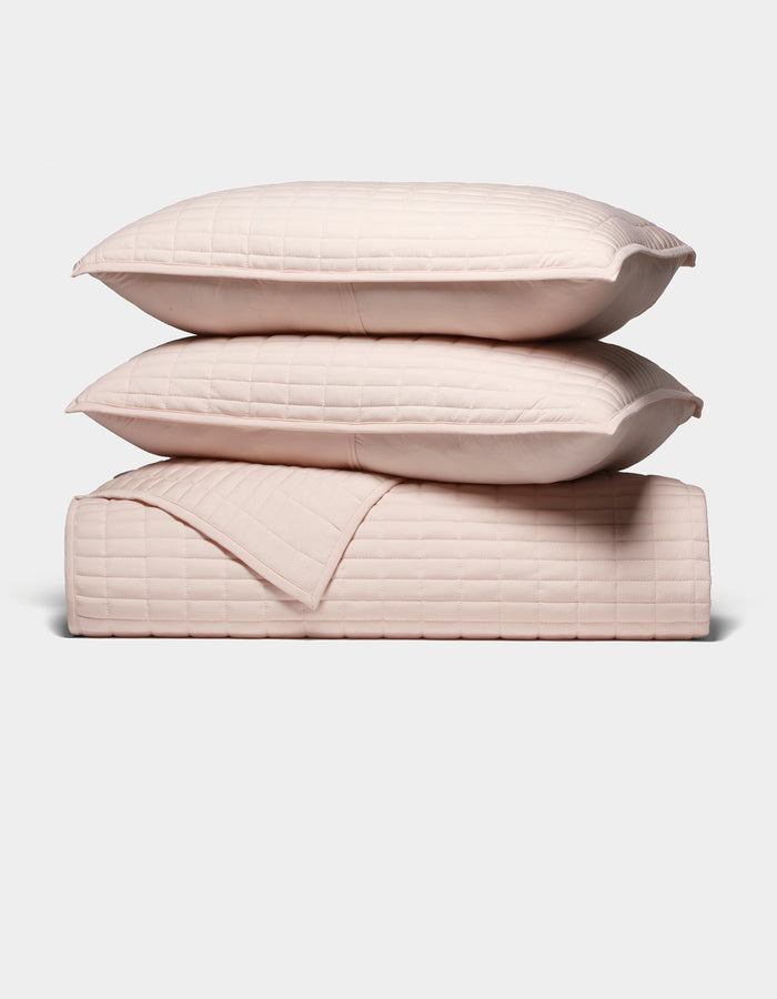 The Cozy Earth Bamboo Jersey Quilt Bundle features two light pink quilted pillows stacked atop a matching quilted blanket, all neatly arranged against a plain white background.|Color:Petal