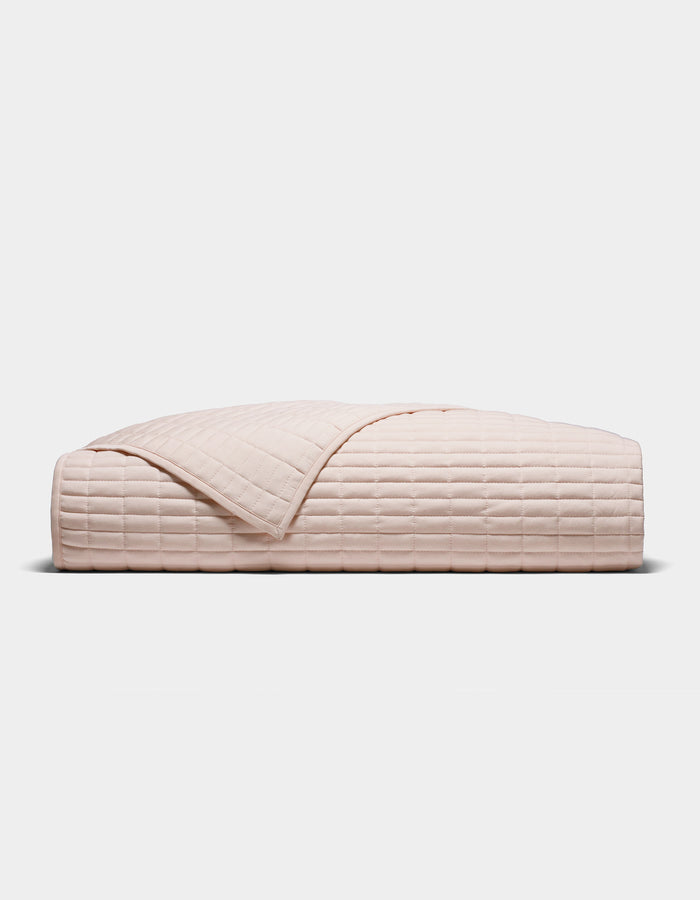 The Cozy Earth Bamboo Jersey Quilt, shown folded in blush-pink with a quilted grid pattern, is displayed against a plain white background.|Color:Petal