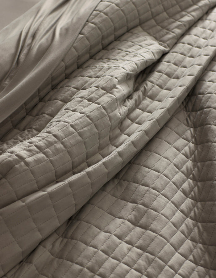 Close-up of the Cozy Earth Bamboo Jersey Quilt in light gray, featuring a quilted grid pattern with visible folds and soft texture for a cozy, inviting look.|Color:Stone