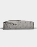 A neatly made bed features the Cozy Earth Bamboo Quilt in smooth, shiny silver-gray satin, partially folded back at the top, set against a plain white background.|Color:Charcoal