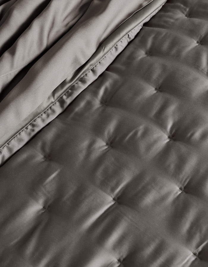 A close-up of the Cozy Earth Bamboo Quilt, neatly folded, showcasing its quilted dark gray design with smooth, satin-like texture and square stitching.|Color:Charcoal
