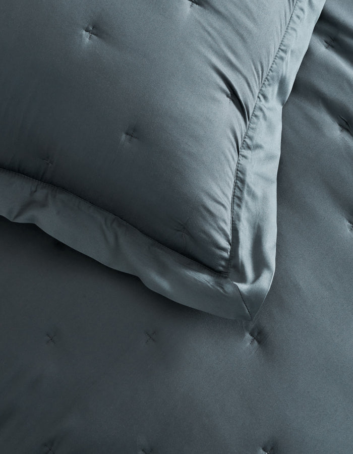 A close-up of a neatly made bed featuring Cozy Earth Bamboo Quilted Shams in dark gray, each with small tufted stitches.|Color:Pacific Blue