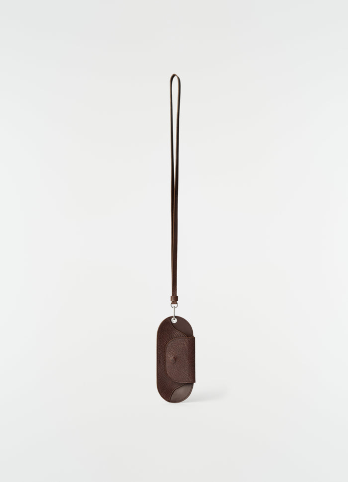 Glasses case in glossy dark brown vegetable-tanned leather with strap by LEMAIRE on plain white background