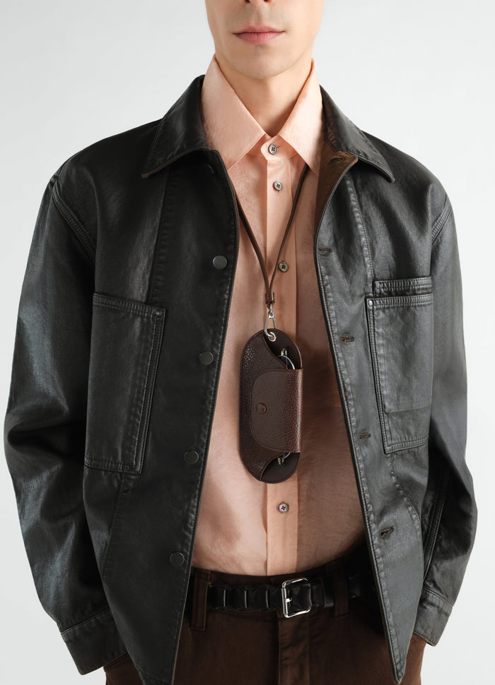 Glasses case in brown glossy vegetable-tanned leather by LEMAIRE worn by a model with a black leather jacket