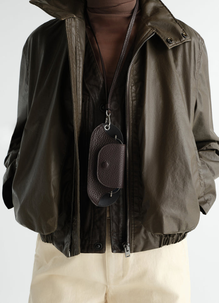 Glasses case in dark brown glossy vegetable-tanned leather by LEMAIRE worn by model front close-up