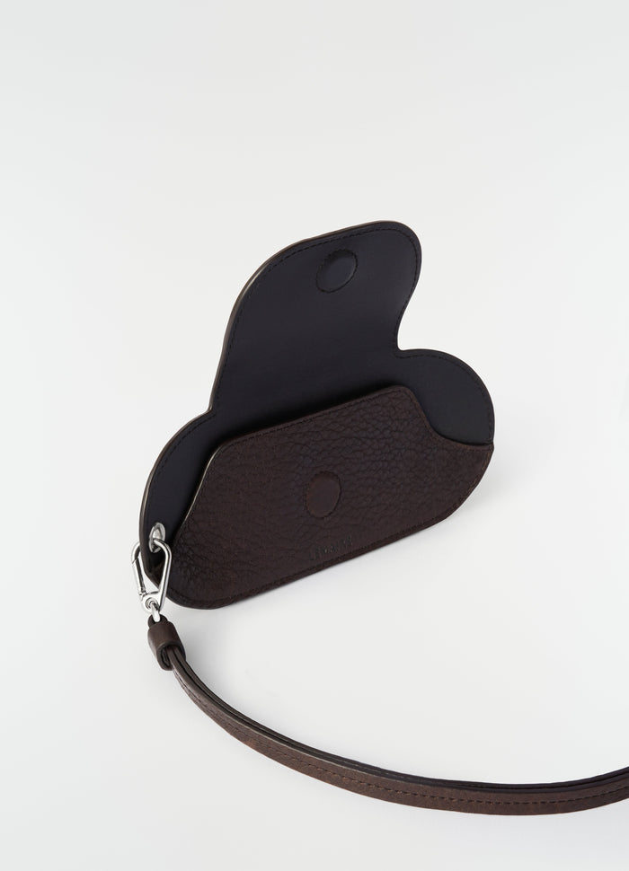 Glasses case in dark brown glossy vegetable-tanned leather by LEMAIRE open front view with wrist strap on white background