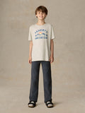 Child wearing a grey surf & ski club tee and black pants against a beige background