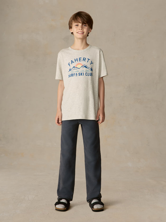 Child wearing a grey surf & ski club tee and black pants against a beige background