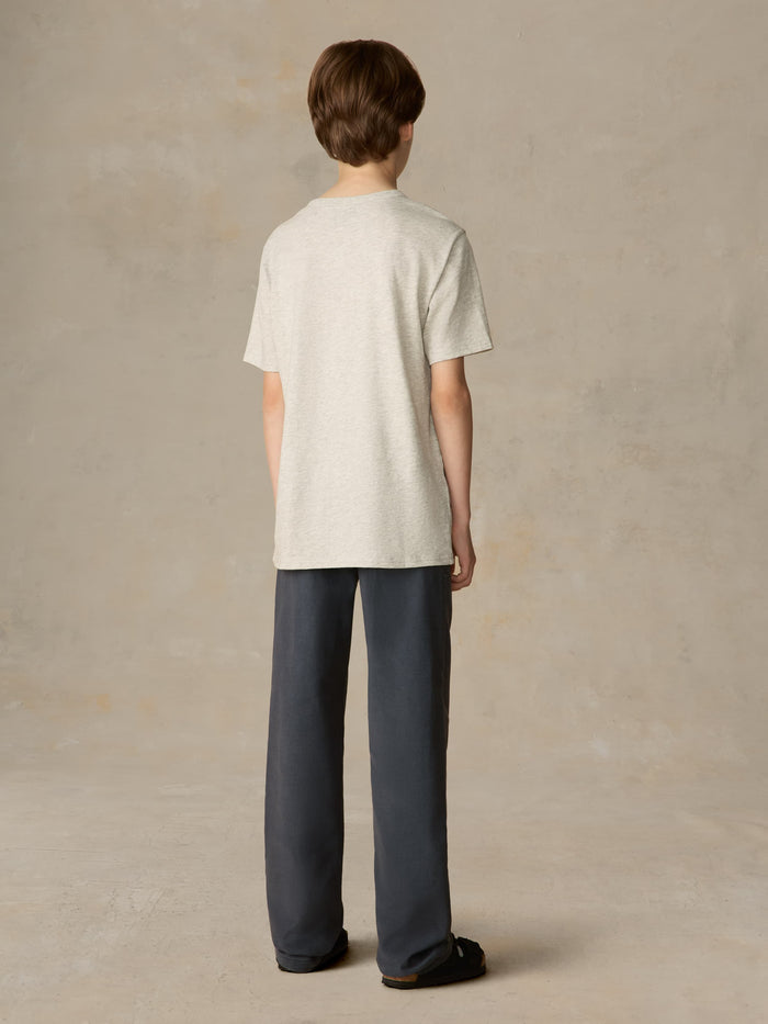 Child wearing a grey surf & ski club tee and black pants against a beige background