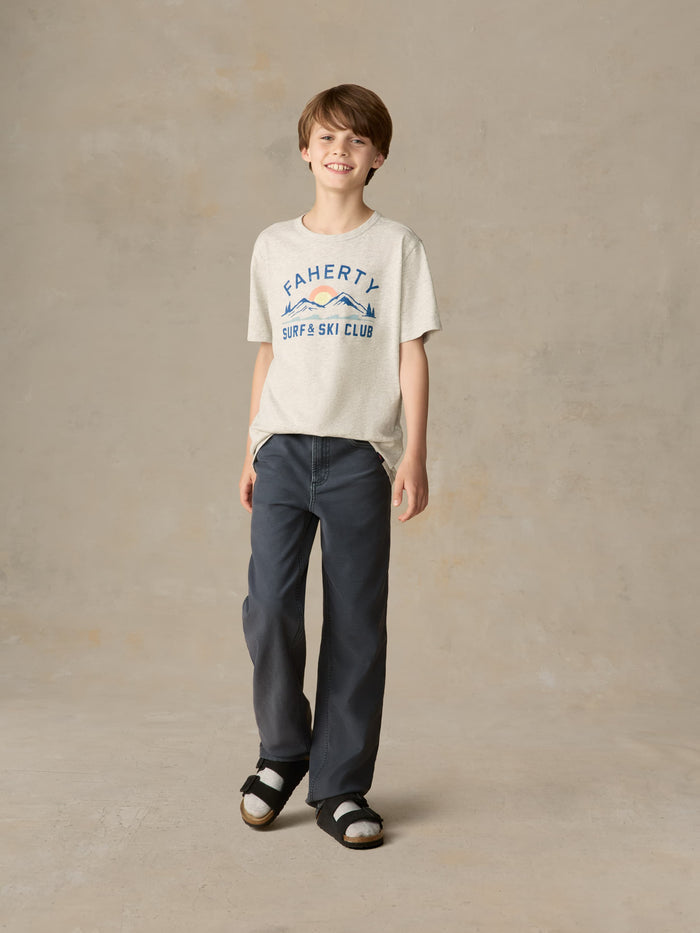 Child wearing a grey surf & ski club tee and black pants against a beige background