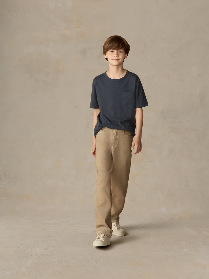 Child wearing a blue t-shirt and beige pants against a beige background