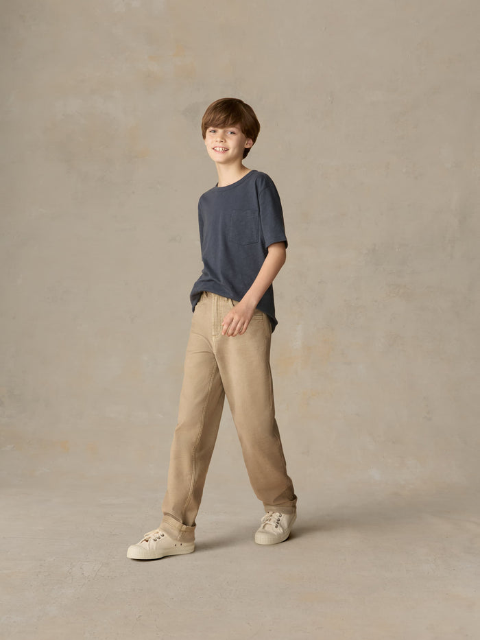 Child wearing a blue t-shirt and beige pants against a beige background