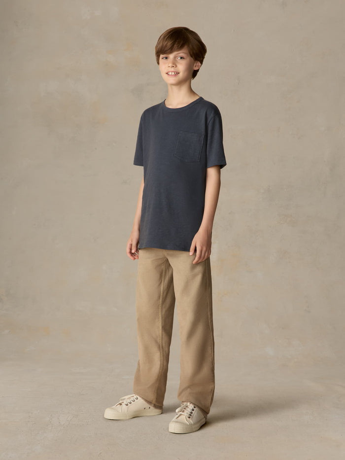 Child wearing a blue t-shirt and beige pants against a beige background
