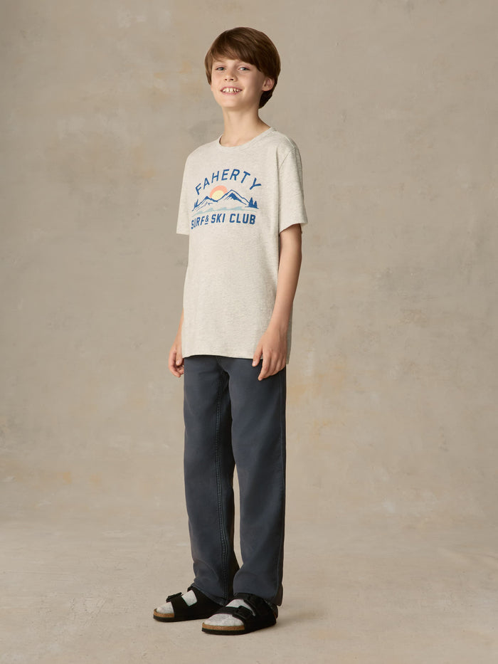Child wearing a grey graphic tee with navy pants against a beige background