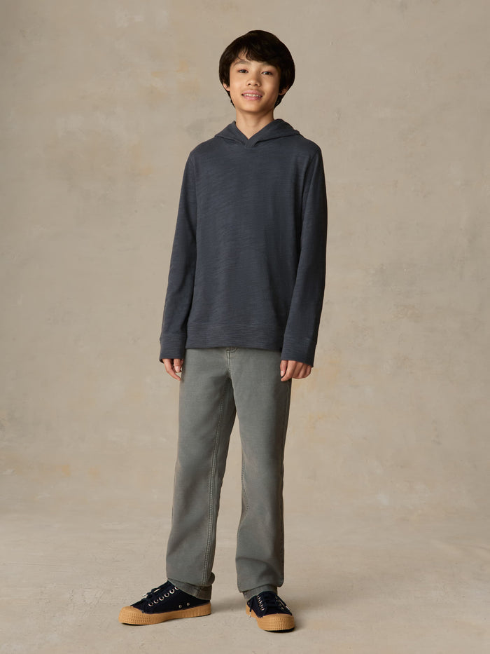 Child wearing a navy hoodie and grey pants against a beige background