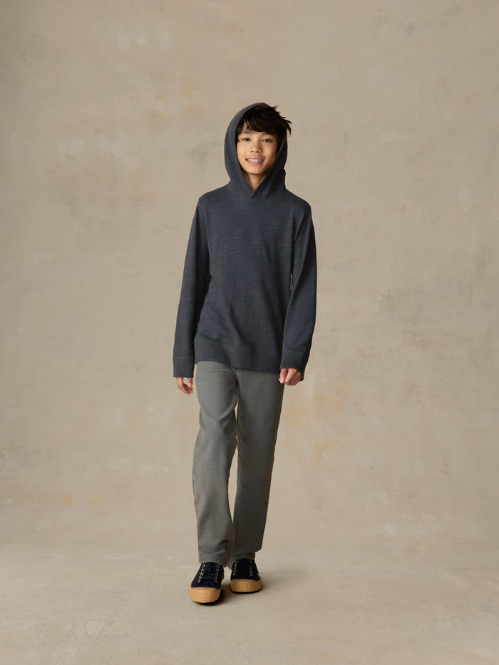 Child wearing a navy hoodie and grey pants against a beige background