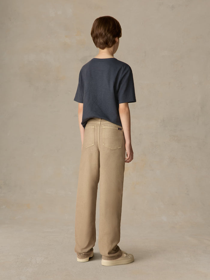 Child wearing a blue pocket tee and beige pants against a beige background