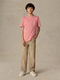 Child wearing a red pocket tee and beige pants against a beige background