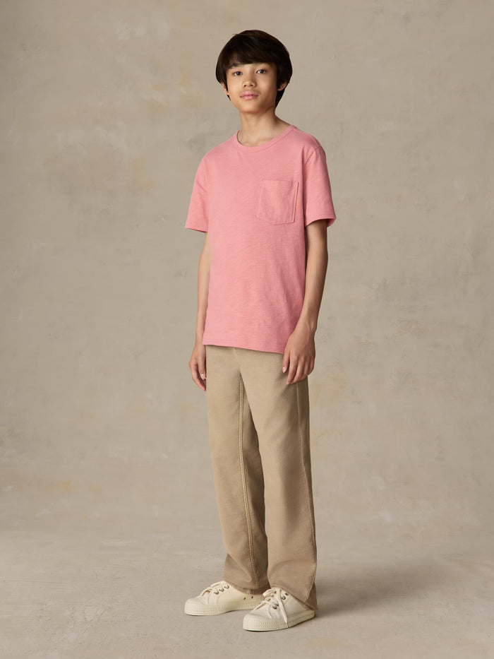 Child wearing a red pocket tee and beige pants against a beige background