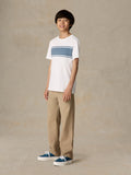 Child wearing a white shirt with blue stripe and beige pants against a beige background