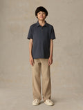 Child wearing a blue polo shirt and beige pants against a beige background