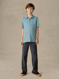 Child wearing a light blue polo and navy pants against a beige background