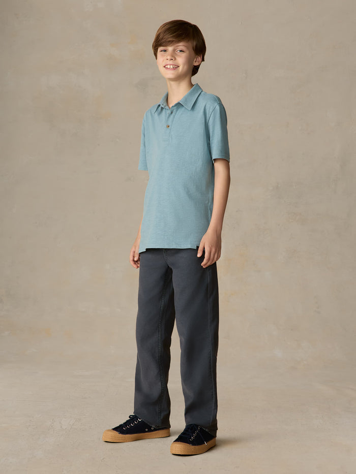 Child wearing a light blue polo and navy pants against a beige background