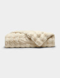 The Cozy Earth Bubble Cuddle Blanket is a folded, cream-colored faux fur throw with a soft, plush texture, shown against a plain white background.|Color:Creme