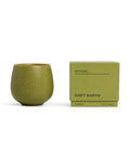 A green ceramic Candle BOTANIC by Cozy Earth sits beside its matching box, labeled with "garden basil, mint leaves, blonde woods" and "9.2 OZ | 260 G.