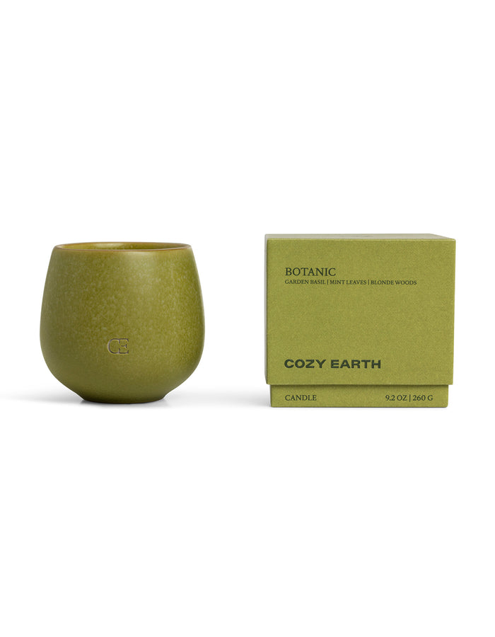 A green ceramic Candle BOTANIC by Cozy Earth sits beside its matching box, labeled with "garden basil, mint leaves, blonde woods" and "9.2 OZ | 260 G.