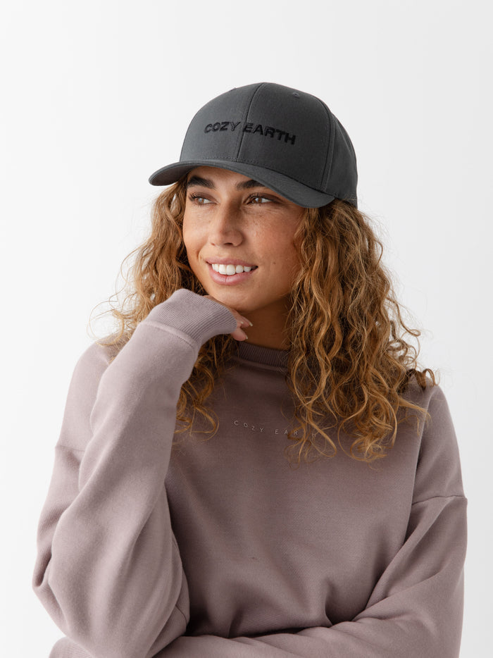 A woman wearing a grey cap with 'COZY EARTH' text on a white background |Color:Charcoal/Black