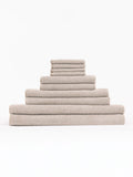 The Complete Nantucket Bath Bundle by Cozy Earth, featuring beige textured towels in various sizes, is neatly stacked pyramid-style on a white background.|Color:Heathered Sand