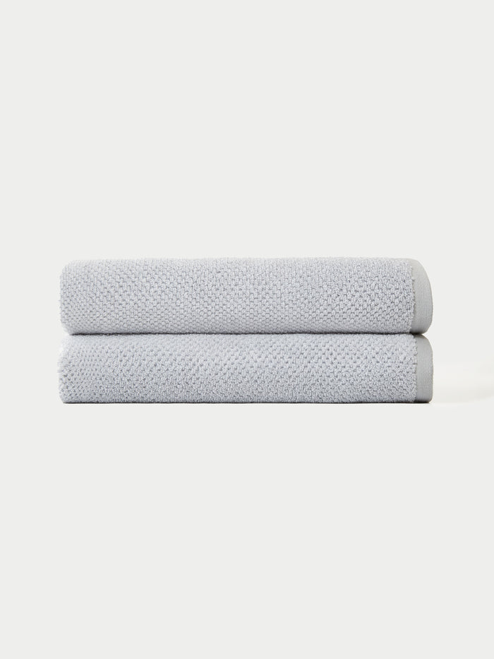 The Complete Nantucket Bath Bundle by Cozy Earth features two neatly folded light gray towels stacked on top of each other against a plain white background.|Color:Heathered Harbor Mist