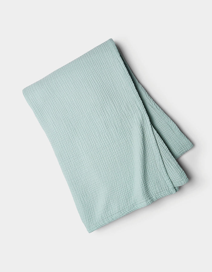 The Cozy Earth Cotton Gauze Blanket, in light blue with a textured finish, is neatly folded and displayed on a plain white background.|Color:Tide