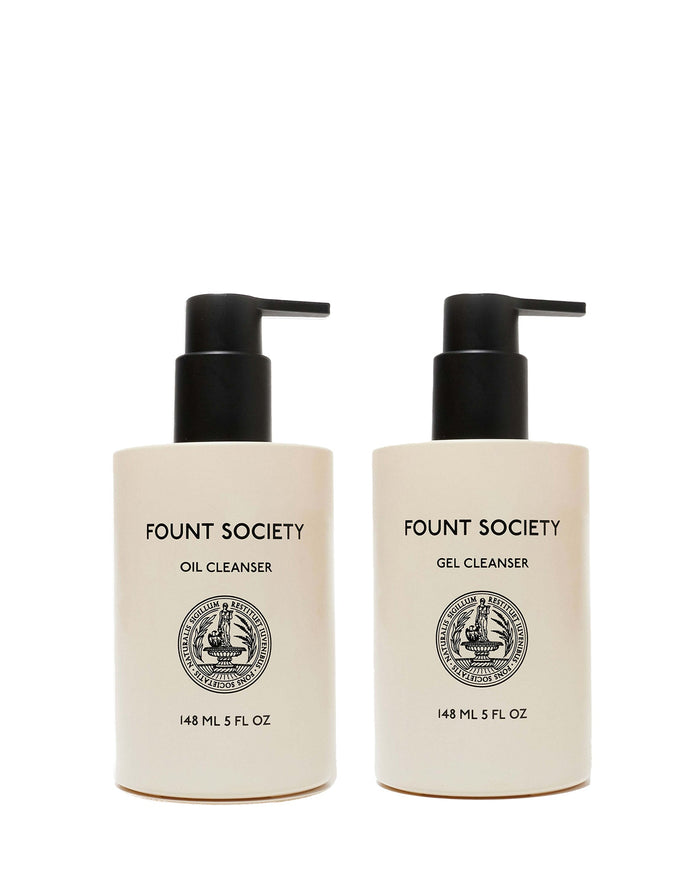 Two beige pump bottles from Cozy Earth’s Double Cleanse Duo—Oil Cleanser on the left, Gel Cleanser on the right—feature black pumps, black text, round front emblems, and each holds 148 mL (5 fl oz).