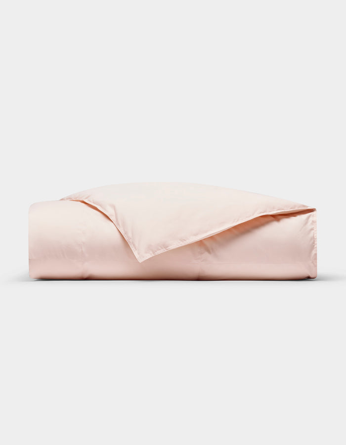 The Cozy Earth Down Alternative Throw in light pink is neatly folded against a white background, with one corner turned back to reveal its soft texture.|Color:Petal